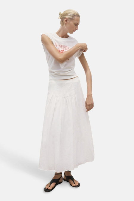 Wit T-shirt met korte mouwen van MANGO, gedragen met een lange witte rok en zwarte sandalen.