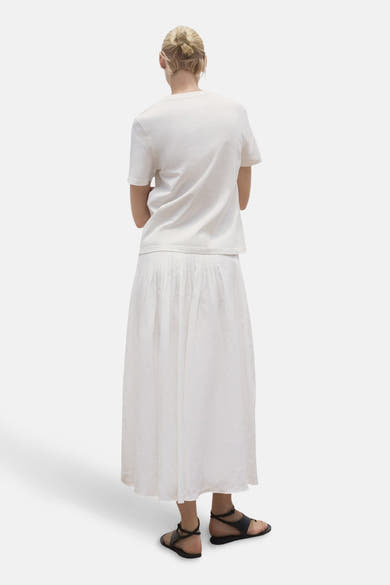 Wit T-shirt met korte mouwen van MANGO, gedragen met een lange geplooide rok en zwarte sandalen.