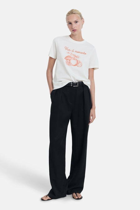 Wit T-shirt met korte mouwen van MANGO, versierd met een illustratie en de tekst "Vivi il momento", gedragen met een zwarte broek.