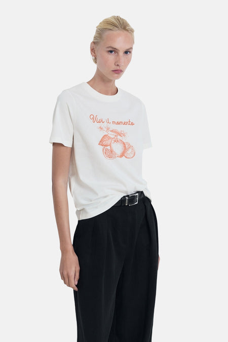 Wit T-shirt met korte mouwen van MANGO, met oranje opschrift en citrusvruchtenmotief, gedragen met een zwarte broek.