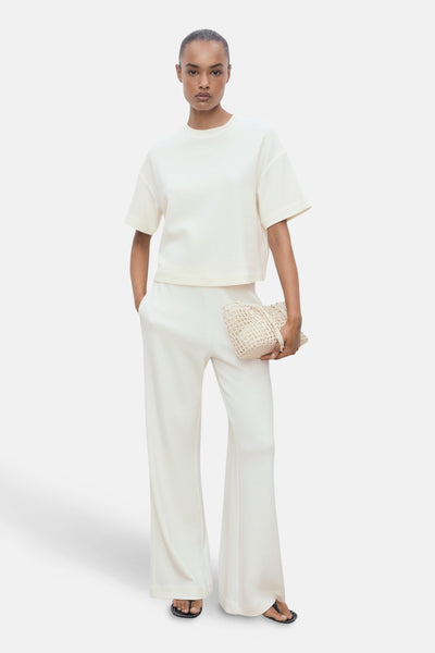 T-shirt écru à manches courtes de MANGO, porté avec un pantalon large et un sac en maille.