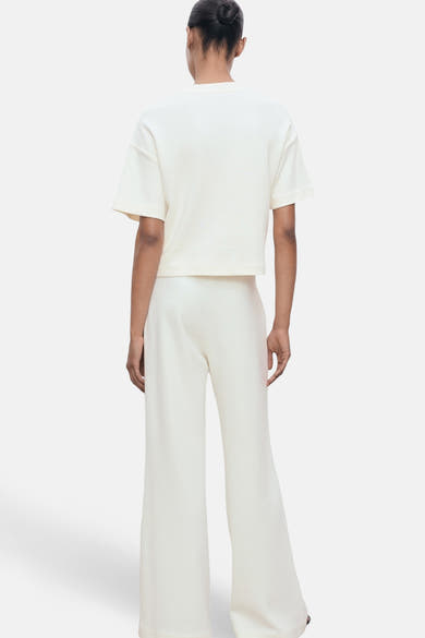 T-shirt écru à manches courtes de MANGO, porté avec un pantalon ample blanc, vue de dos.