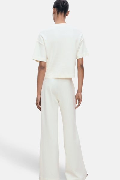 T-shirt écru à manches courtes de MANGO, porté avec un pantalon ample blanc, vue de dos.