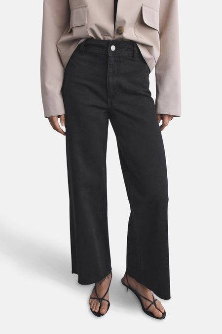 Jean large en denim noir de MANGO, porté avec un blazer beige et des sandales à brides.
