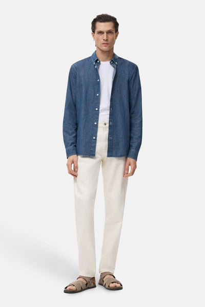 Denim overhemd met lange mouwen van MANGO, gedragen met een wit T-shirt en een crèmekleurige broek.