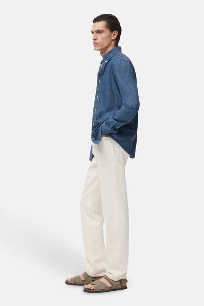 Denim overhemd met lange mouwen van MANGO, gedragen met een gebroken witte broek en bruine sandalen, van opzij gezien.