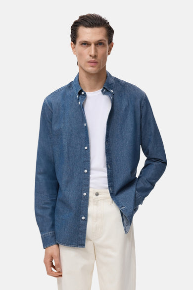 Blauwe spijkerblouse met lange mouwen van MANGO, gedragen open over een wit T-shirt en een beige broek.