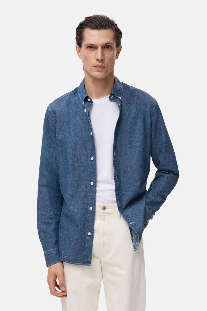 Blauwe spijkerblouse met lange mouwen van MANGO, gedragen open over een wit T-shirt en een beige broek.