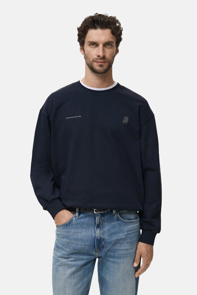 Marineblauwe trui van MANGO, met discreet logo en gedragen met een lichte spijkerbroek.