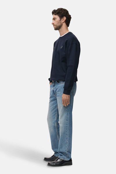 Blauwe trui van MANGO, met witte ronde hals, gedragen met een lichte spijkerbroek en zwarte loafers.
