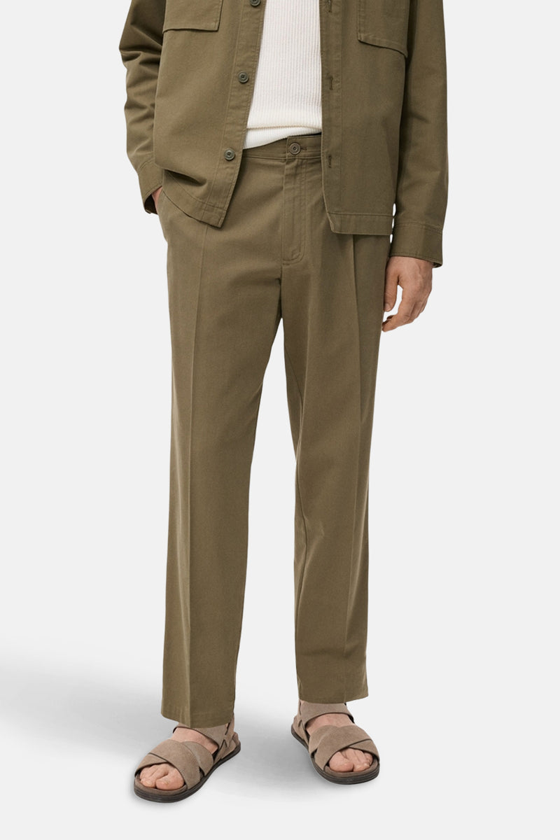 Pantalon kaki de MANGO, coupe droite avec plis, porté avec une veste et des sandales beiges.