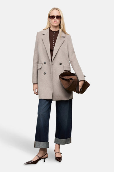Veste longue marron par MANGO, avec un design croisé, portée avec un cardigan marron, un jean et des escarpins à talons.