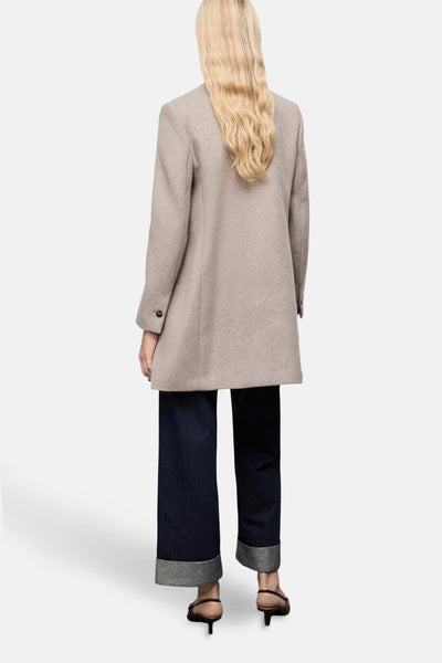Veste longue marron de MANGO, vue de dos, portée avec un pantalon large bleu marine à revers et des talons.