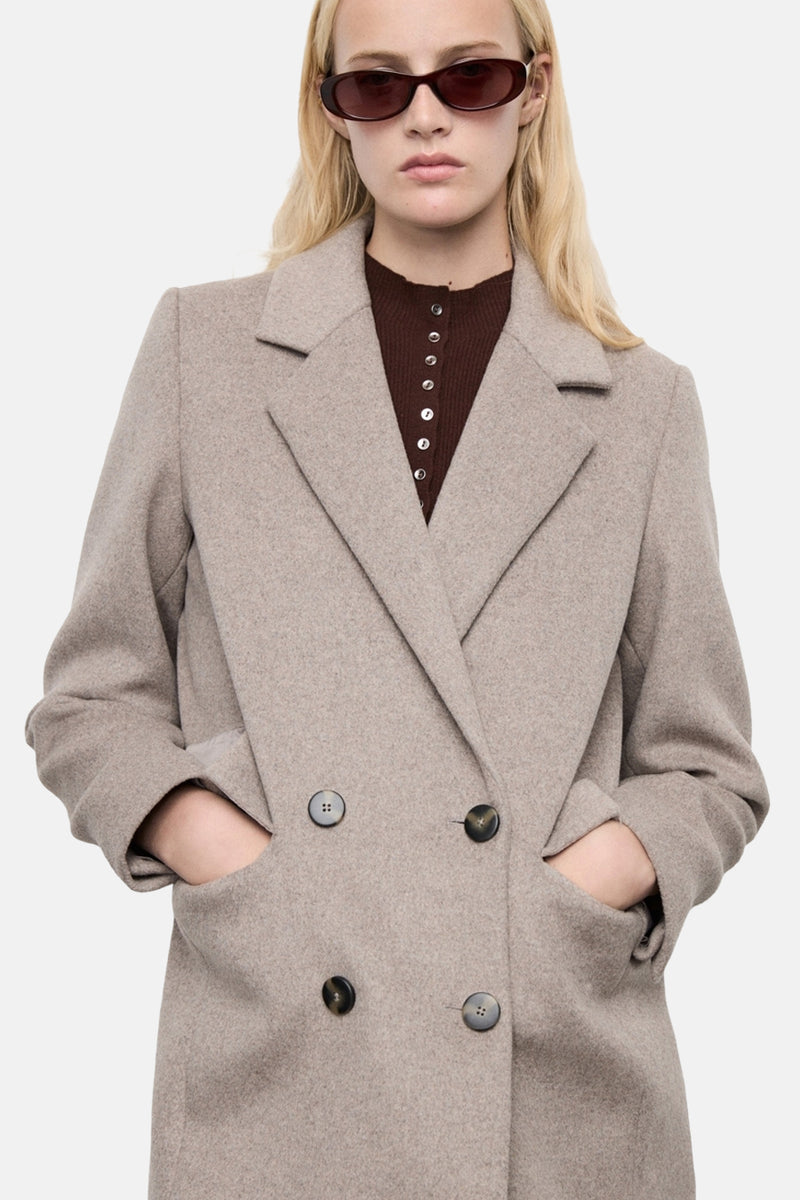 Veste longue marron de MANGO avec boutonnage croisé et mains dans les poches.
