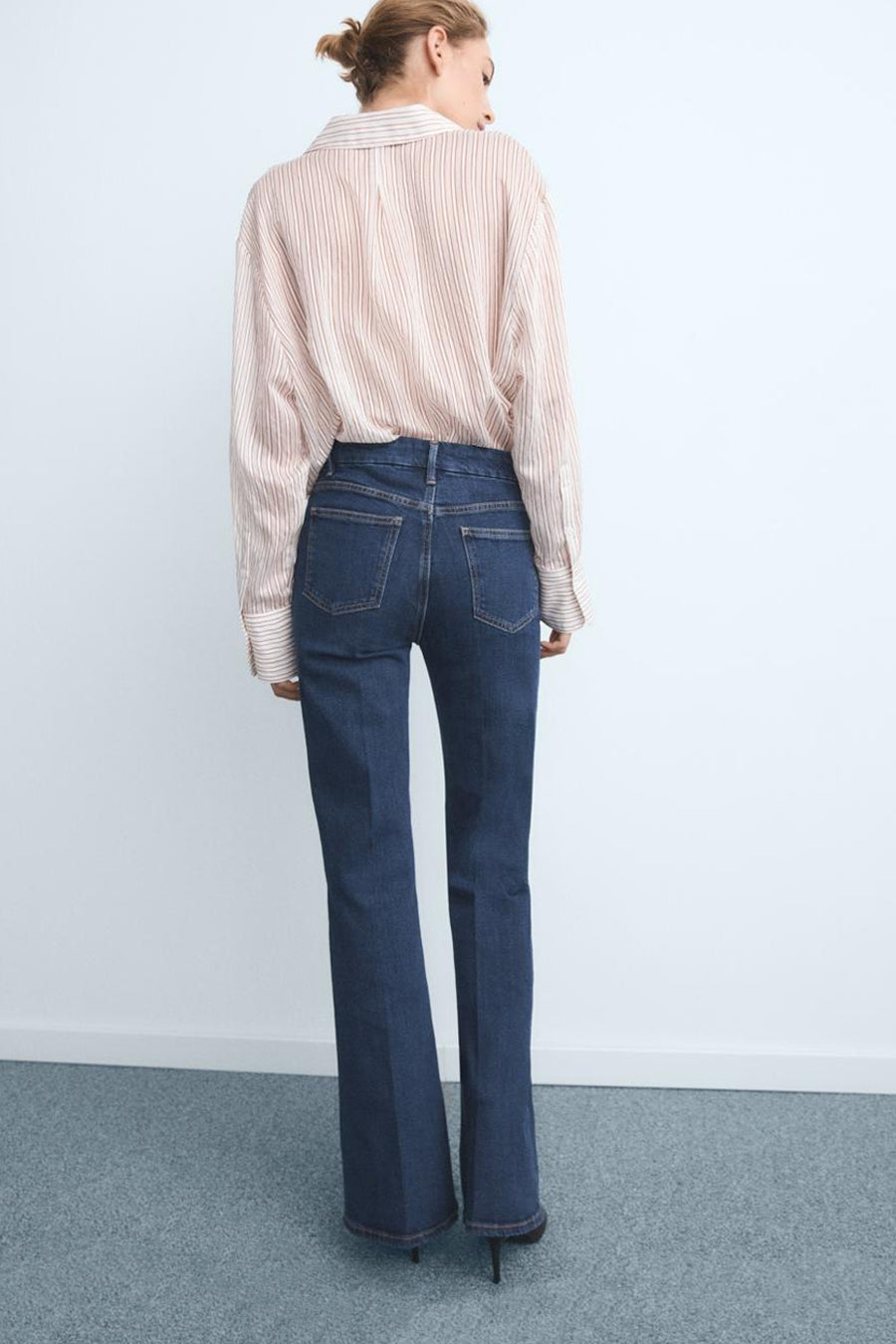 Donkerblauwe flared jeans van MANGO, achterkant, gedragen met een gestreept overhemd.