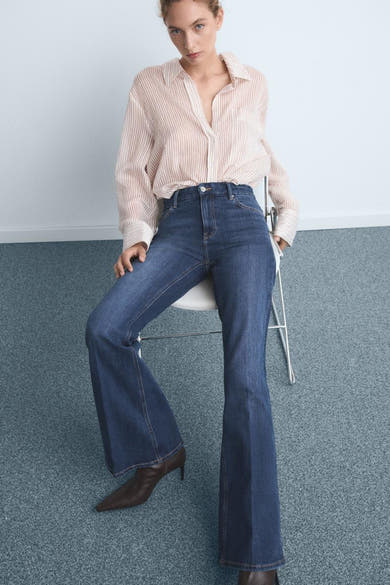 Wijde spijkerbroek in donkerblauw denim van MANGO, gedragen met een gestreept overhemd en bruine enkellaarsjes.