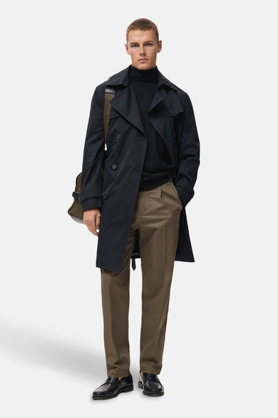 Zwarte rondehals-trui van MANGO, gedragen met een marineblauwe trenchcoat en een bruine broek.