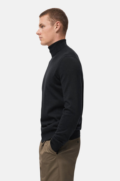 Zwarte trui met ronde hals van MANGO, gedragen met een bruine chino, in profielaanzicht.