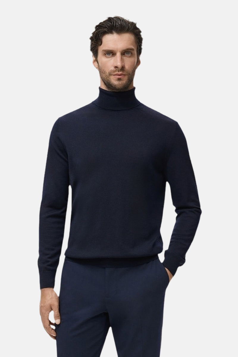 Blauwe trui met ronde hals van MANGO, gedragen met een bijpassende broek, de man poseert met één hand in zijn zak.