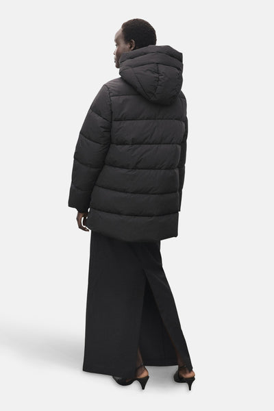 Zwarte lange jas van MANGO, met capuchon, gedragen met een lange zwarte jurk met split en zwarte pumps.