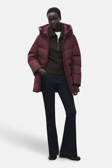 Lange bordeaux jas van MANGO, met capuchon en ritssluiting, gedragen met een bruine trui en een blauwe jeans.
