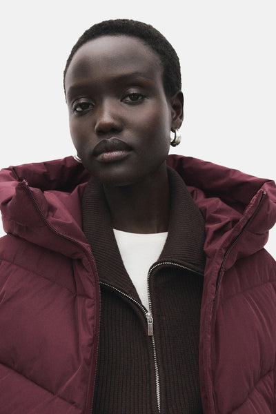 Veste longue bordeaux de MANGO avec capuche, portée sur un cardigan marron et un t-shirt blanc.