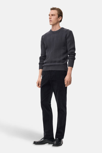 Pull à col rond gris de MANGO, motif à chevrons discret, porté avec un pantalon en velours côtelé noir et des mocassins.