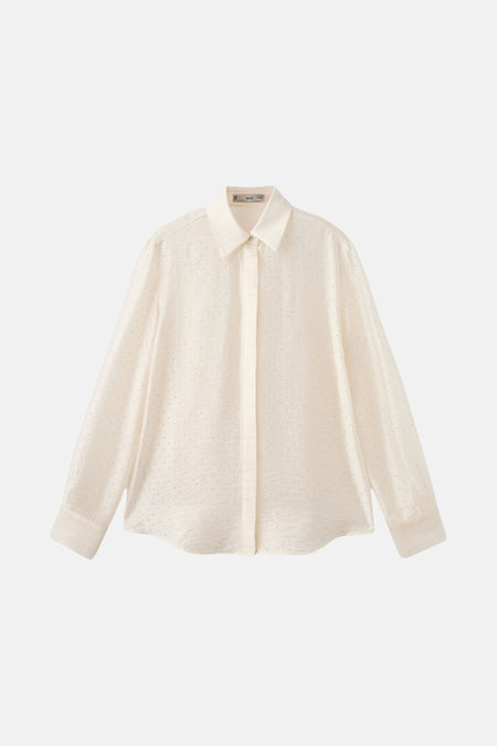 Ecru blouse met lange mouwen van MANGO, met een subtiele textuur, gedragen met een bijpassende vloeiende broek en gouden manchetten.