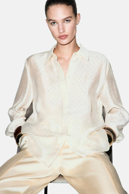 Chemise à manches longues écru de MANGO, à pois discrets et manches retroussées avec bracelets dorés.
