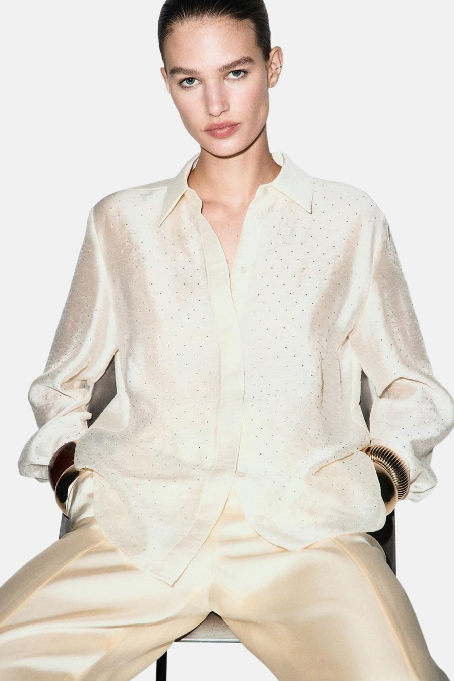 Chemise à manches longues écru de MANGO, à pois discrets et manches retroussées avec bracelets dorés.
