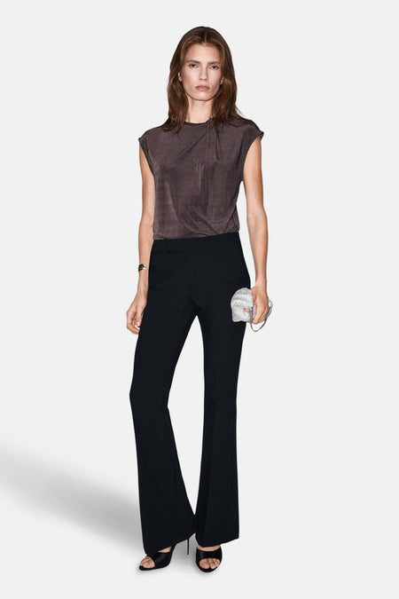 Blouse à manches courtes marron par MANGO, avec un nœud subtil et portée avec un pantalon noir évasé et une pochette argentée.