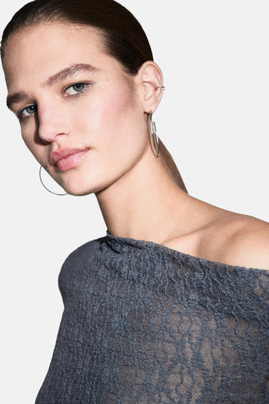 Blouse à manches longues grise de MANGO, en dentelle florale transparente avec un décolleté asymétrique.