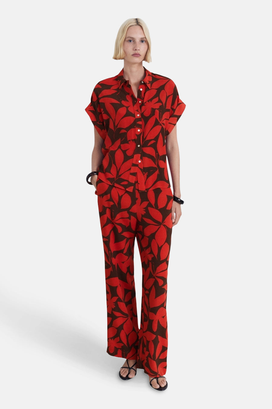 Multikleuren bedrukte broek van MANGO, uitlopend model, rood en bruin bladmotief, gedragen met een bijpassend overhemd.