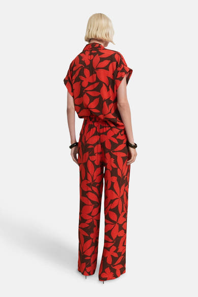 Multikleurige broek van MANGO, met rood en bruin bloemenpatroon, gedragen met zwarte armbanden.