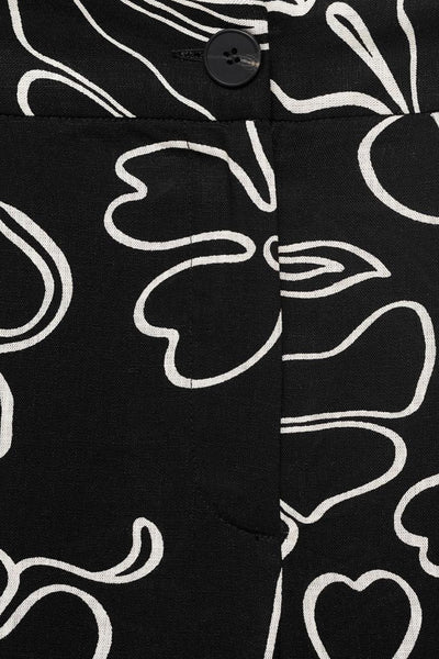 Pantalon noir à motifs floraux blancs par MANGO, avec bouton apparent et coupe ajustée.