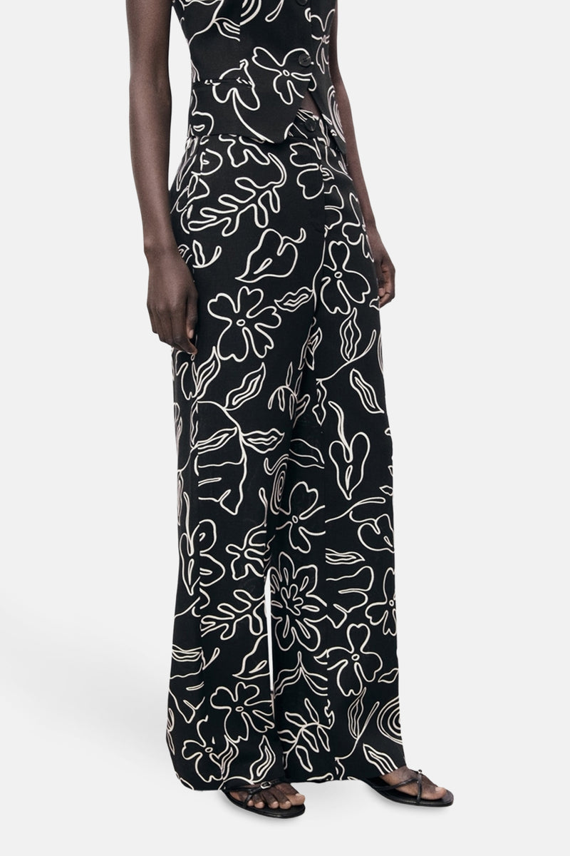 Zwarte broek met wit bloemenpatroon van MANGO, wijde pasvorm, gedragen met een bijpassend topje en sandalen.