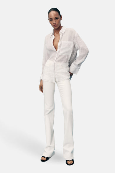 Witte uitlopende jeans van MANGO, gedragen met een wit linnen overhemd en zwarte sandalen.