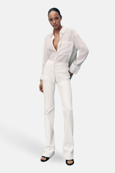 Witte uitlopende jeans van MANGO, gedragen met een wit linnen overhemd en zwarte sandalen.