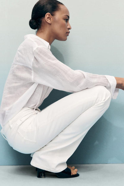 Jean évasé blanc en denim de MANGO, porté avec une chemise blanche transparente et des mules noires à talons.