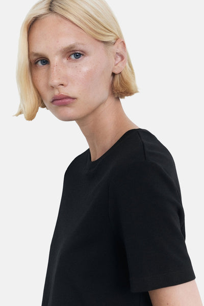 T-shirt noir à manches courtes de MANGO, porté par un mannequin aux cheveux blonds.
