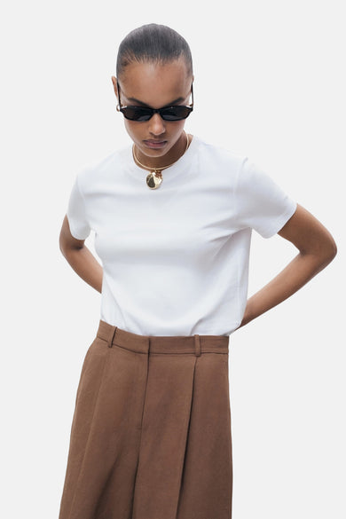 Wit T-shirt met korte mouwen van MANGO, gedragen met een bruine broek met hoge taille en een gouden ketting.