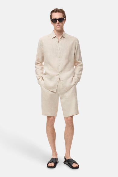 Beige linnen blouse met lange mouwen van MANGO, gedragen met een beige korte broek en zwarte sandalen.