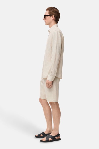 Chemise à manches longues beige de MANGO, portée avec un short assorti et des sandales noires, vue de côté.