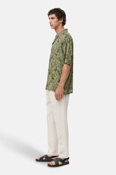 Chemise à manches courtes verte à motifs géométriques par MANGO, portée avec un pantalon beige et des sandales noires.