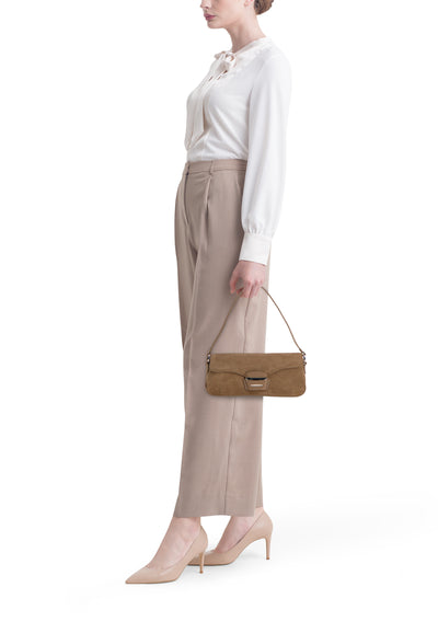 Sac à bandoulière marron en daim, de MANGO, porté avec une chemise blanche à nœud et un pantalon beige.