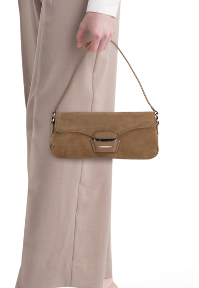 Sac à bandoulière brun de MANGO, porté à la main, avec détails décoratifs et porté avec un pantalon beige.

