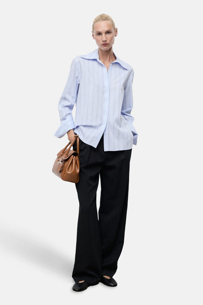 Chemise à manches longues bleue à rayures verticales par MANGO, portée avec un pantalon noir et un sac à main marron.
