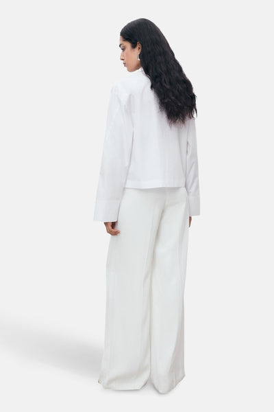 Chemisier à manches longues blanc de MANGO, porté avec un pantalon blanc ample, vue de dos.