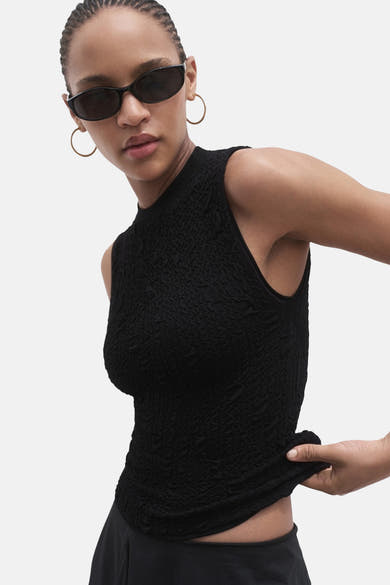 Zwart mouwloos blouse van MANGO, met wafeltextuur, gedragen met een zonnebril en oorringen.
