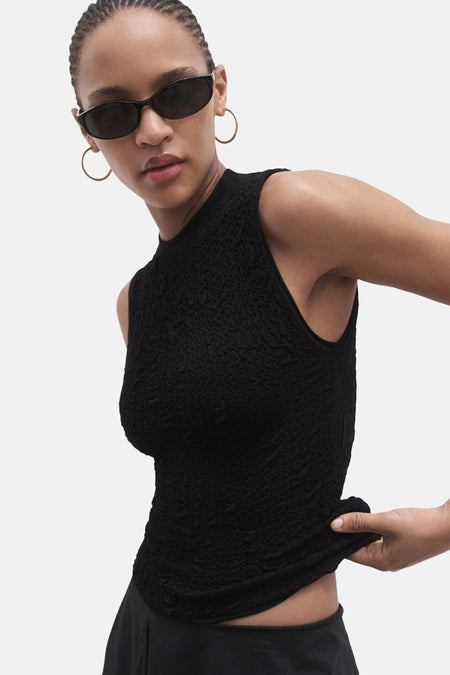 Zwart mouwloos blouse van MANGO, met wafeltextuur, gedragen met een zonnebril en oorringen.